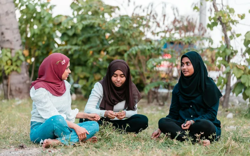 Muslim women sitting on grass in park and talking