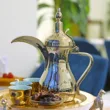 A silver tea pot sits on a tray with a plate of food